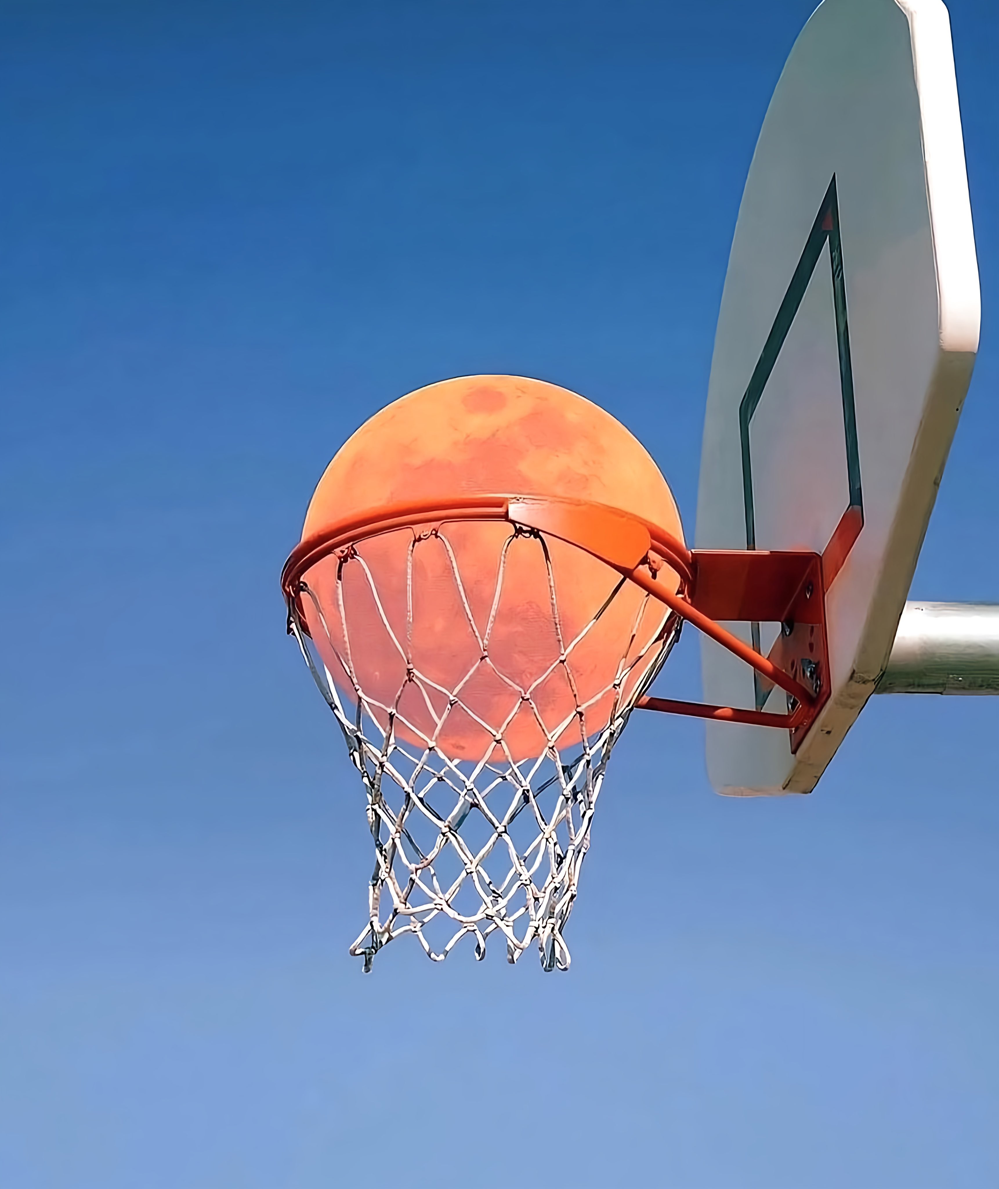 Full Blood Moon in Basketball Hoop Against Blue Sky